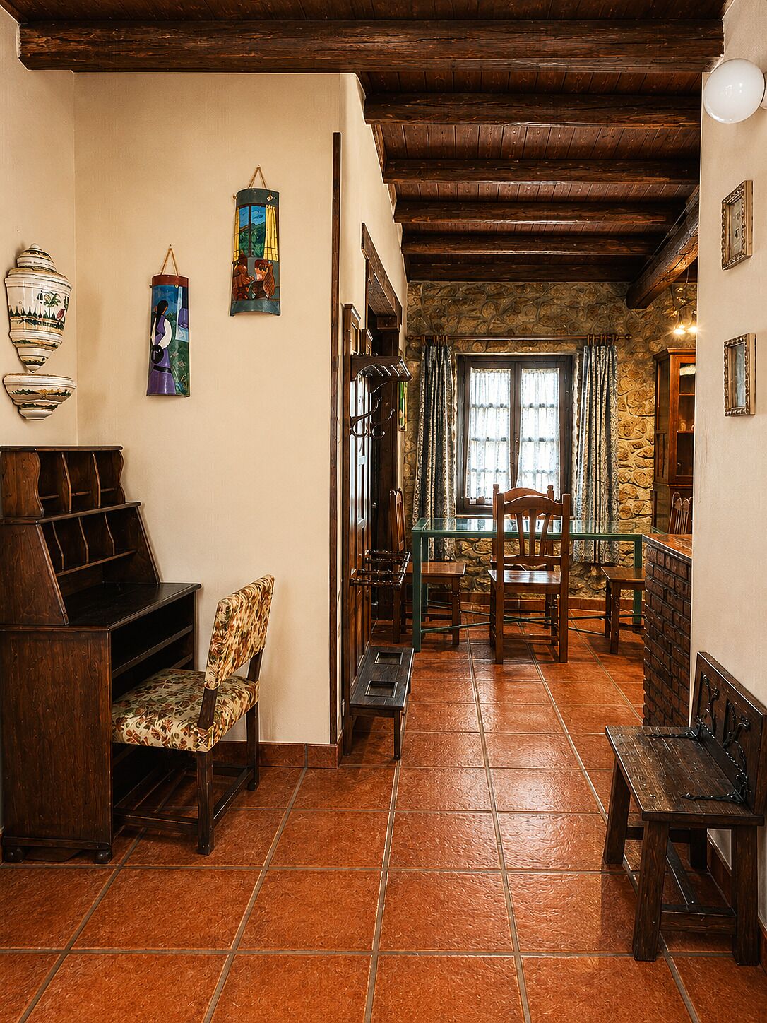 Un interior rústico con una escalera de madera, una zona de comedor con mesa y sillas, y un rincón de estar con una silla y un banco.
