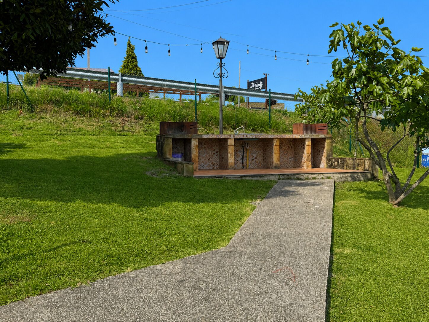 A paved pathway leading to a small outdoor seating area with a metal fence and a lamp post.