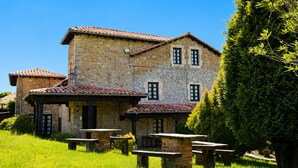 Un bâtiment en pierre avec un toit en tuiles, de nombreuses fenêtres et des places assises à l’extérieur.