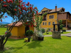 A yellow building with a red roof, surrounded by a well-maintained lawn and various potted plants.