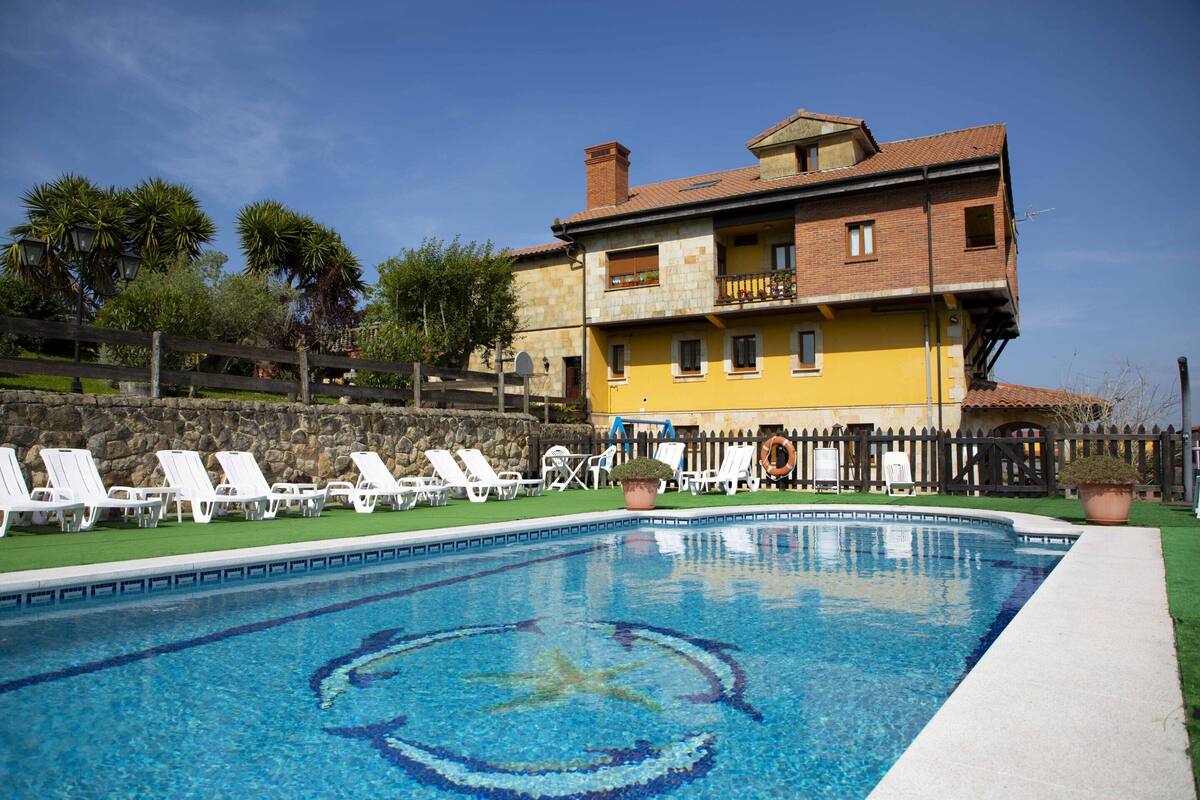 A swimming pool with lounge chairs, a stone wall, and a building with balconies.