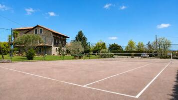 An outdoor tennis court with a stone building in the background.