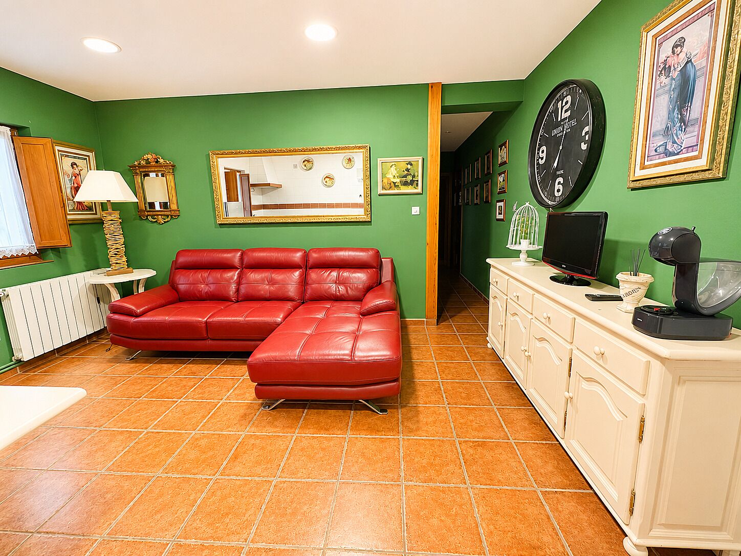 A room with a red leather sofa, a white cabinet, a clock, and a framed picture on the wall.