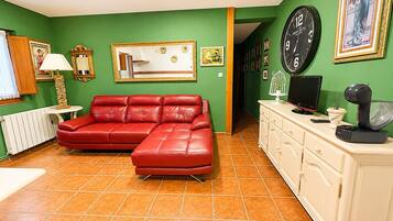A room with a red leather sofa, a white cabinet, a clock, and a framed picture on the wall.
