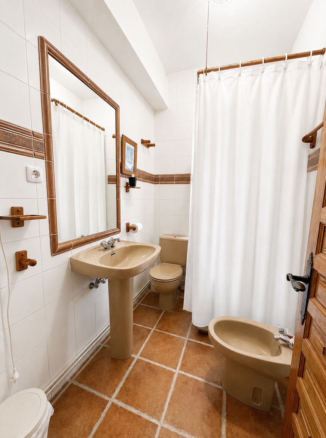 A bathroom with a sink, toilet, and bidet, white tiled walls, and a wooden door.