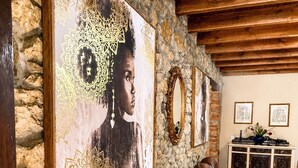 Un mur en pierre agrémenté d’un tableau encadré, un plafond en bois, un canapé en cuir marron, un meuble en bois et un sol carrelé.