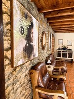 Pared de piedra con un cuadro enmarcado, techo de madera, sofá de cuero marrón, aparador de madera y suelo de baldosas.