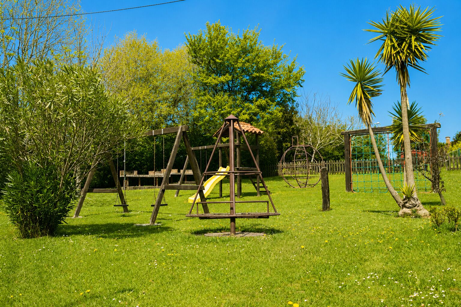 Une balançoire en bois avec un toboggan jaune, installée dans un espace verdoyant, agrémenté d’arbres et surplombé d’un ciel dégagé.