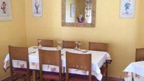 A dining area with a table set for six, surrounded by wooden chairs with red cushions. - Hostal Mónica (Valle De Valdebezana)