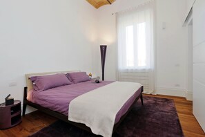 Un dormitorio con cama, una lámpara de noche, una computadora portátil y una mesita con un libro.