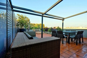 Un patio exterior con cerramiento de vidrio, mobiliario de mimbre y vistas a la ciudad.