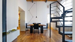 A modern interior with a wooden dining table, black chairs, a black metal staircase, and a bookshelf in the background. - San Lorenzo (Rome)