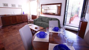 Un comedor con una mesa de madera, platos azules y vasos. Hay un sofá verde y una zona de cocina con armarios de madera.