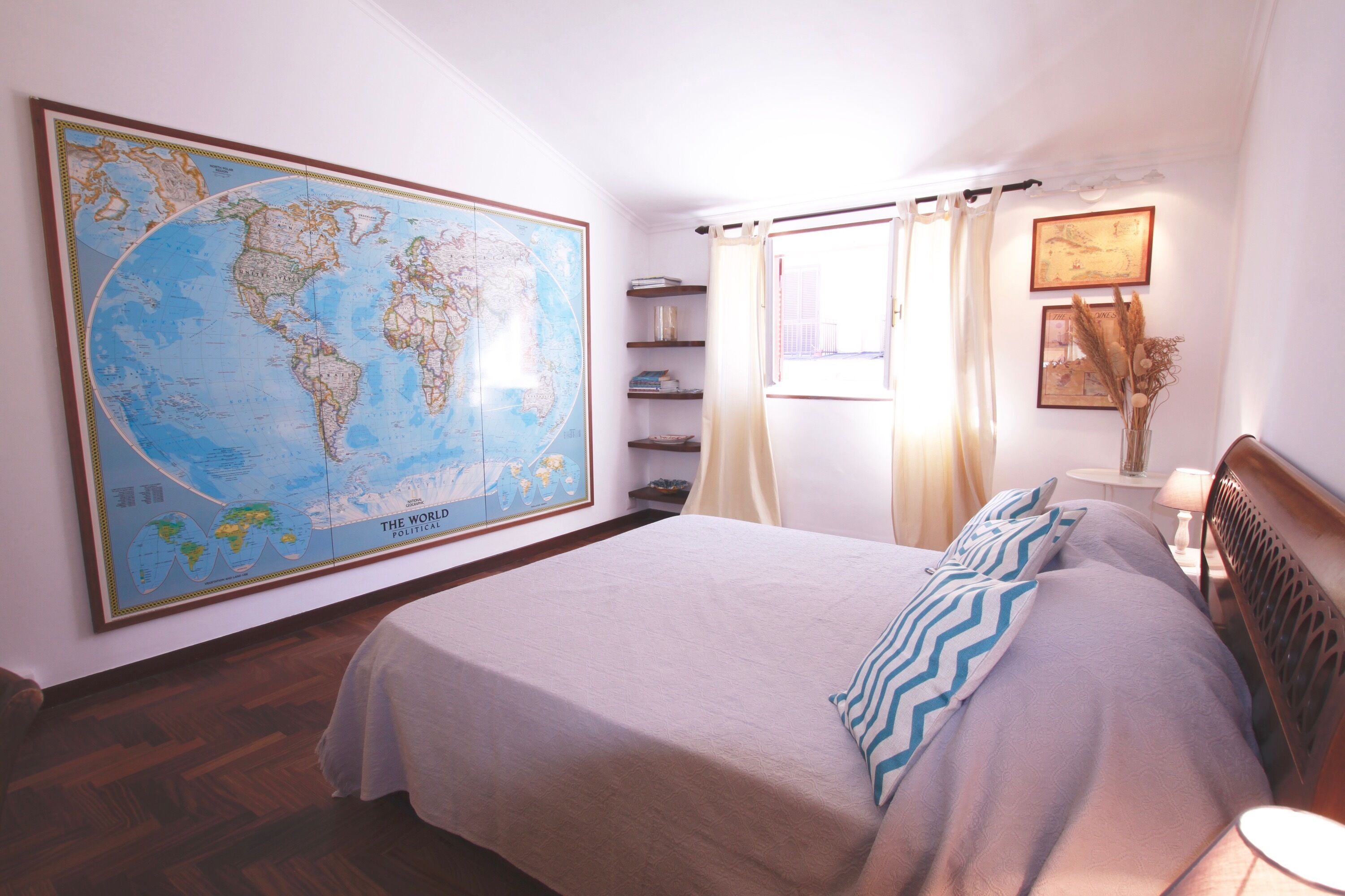 Un dormitorio con un gran mapa del mundo en la pared, una cama con almohada a rayas, cabecero de madera y mesita de noche con lámpara.
