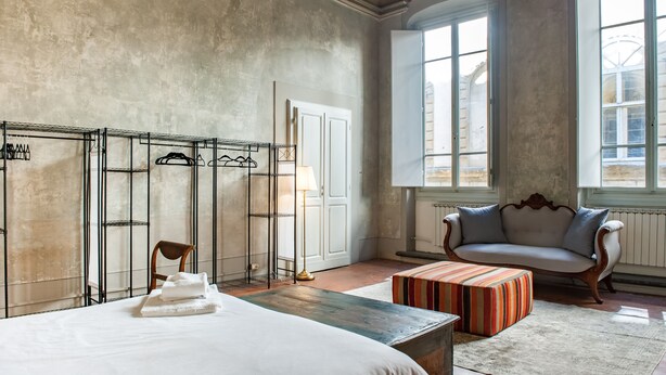 A room with a bed, a sofa, a chair, a radiator, and a window with a view. - Ponte Vecchio Affresco (Florence)