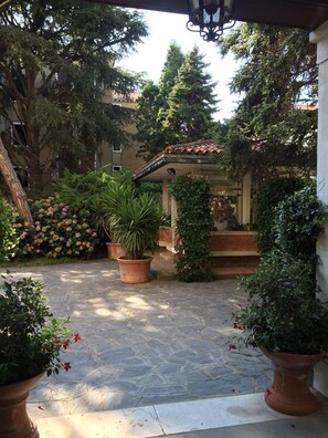 A courtyard with potted plants, a tiled floor, and a building entrance. - Giudecca Garden (Venice)