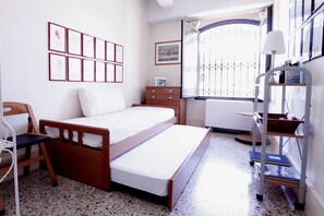 A small, neatly arranged bedroom with a single bed, a wooden dresser, a chair, and a window with a view.