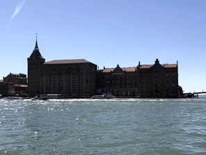 A large, historic building with multiple stories and a prominent tower, located beside a body of water.