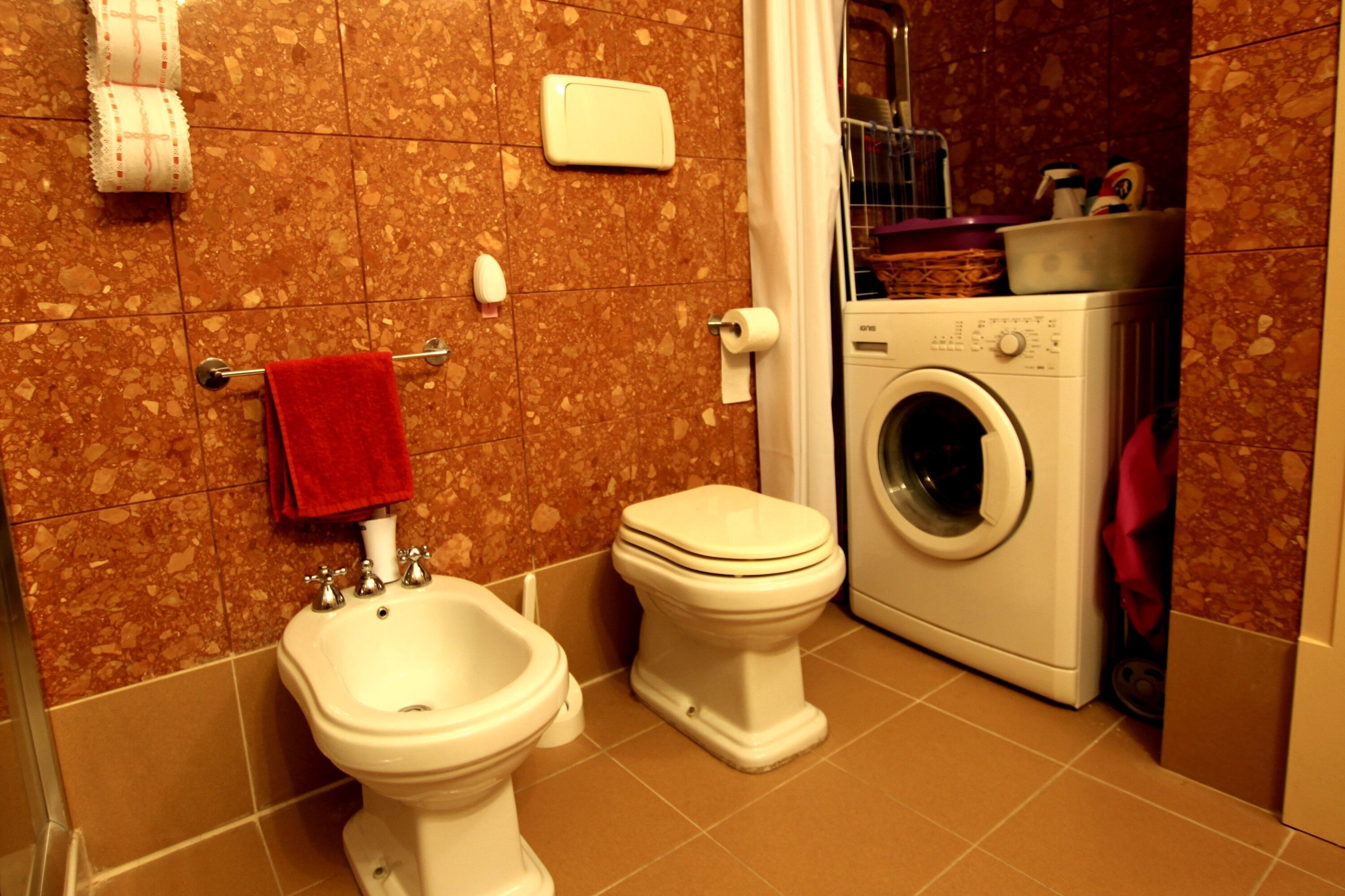 A bathroom with a bidet, toilet, and washing machine.