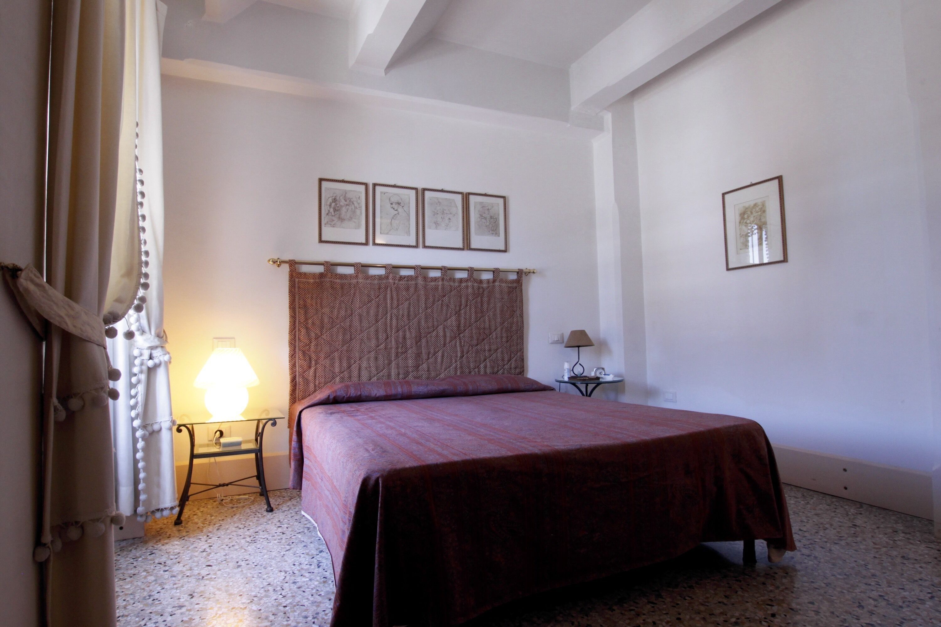 A bedroom with a bed, a nightstand, a lamp, and a wall with framed pictures.