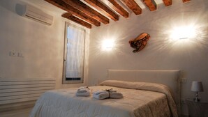 A bedroom with a bed, a wall-mounted light fixture, and a window with a curtain. - San Marcuola Green (Venice)