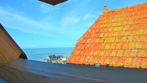 A view from a window overlooking a red-roofed building with a clear blue sky and the sea in the background. - La Belle Aultoise, Ault center, sea view, Baie de Somme (Ault)