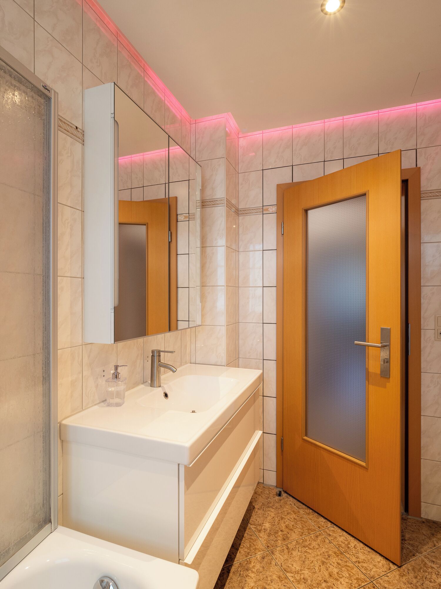A modern bathroom with a large mirror, a white sink, a bathtub, and a wooden door.