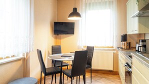 Une cuisine compacte avec un coin repas, un téléviseur fixé au mur et un radiateur placé sous la fenêtre.
