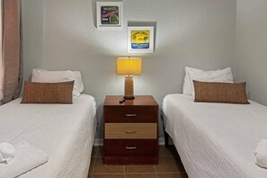 Een hotelkamer met twee bedden, een nachtkastje met een lamp en twee afbeeldingen in lijsten aan de muur.