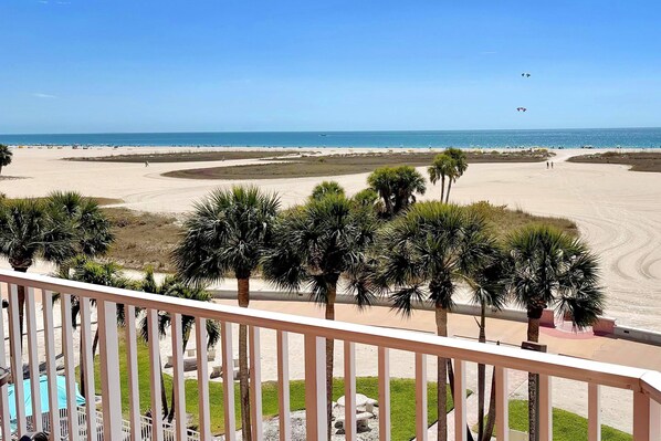 A beach view from a balcony with palm trees and a clear sky.