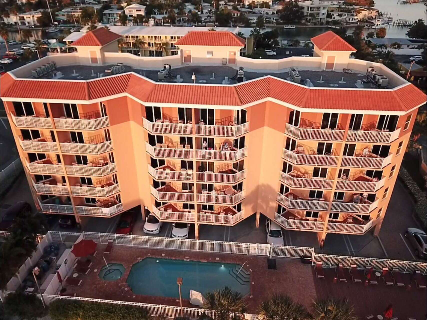 Un hotel de varios pisos con balcones, piscina y un puerto deportivo al fondo.