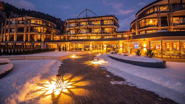 Un hotel modern amb diversos pisos, un pati cobert de neu i zones d'estar a l'exterior il·luminades.