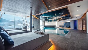 Zona d'una piscina interior moderna amb vistes a les muntanyes, una zona de seients amb coixins i una barra amb prestatgeries.