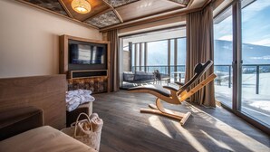 Habitació d'hotel moderna amb una finestra gran, un sostre de fusta, un sofà, una cadira de massatge i una televisió plana.