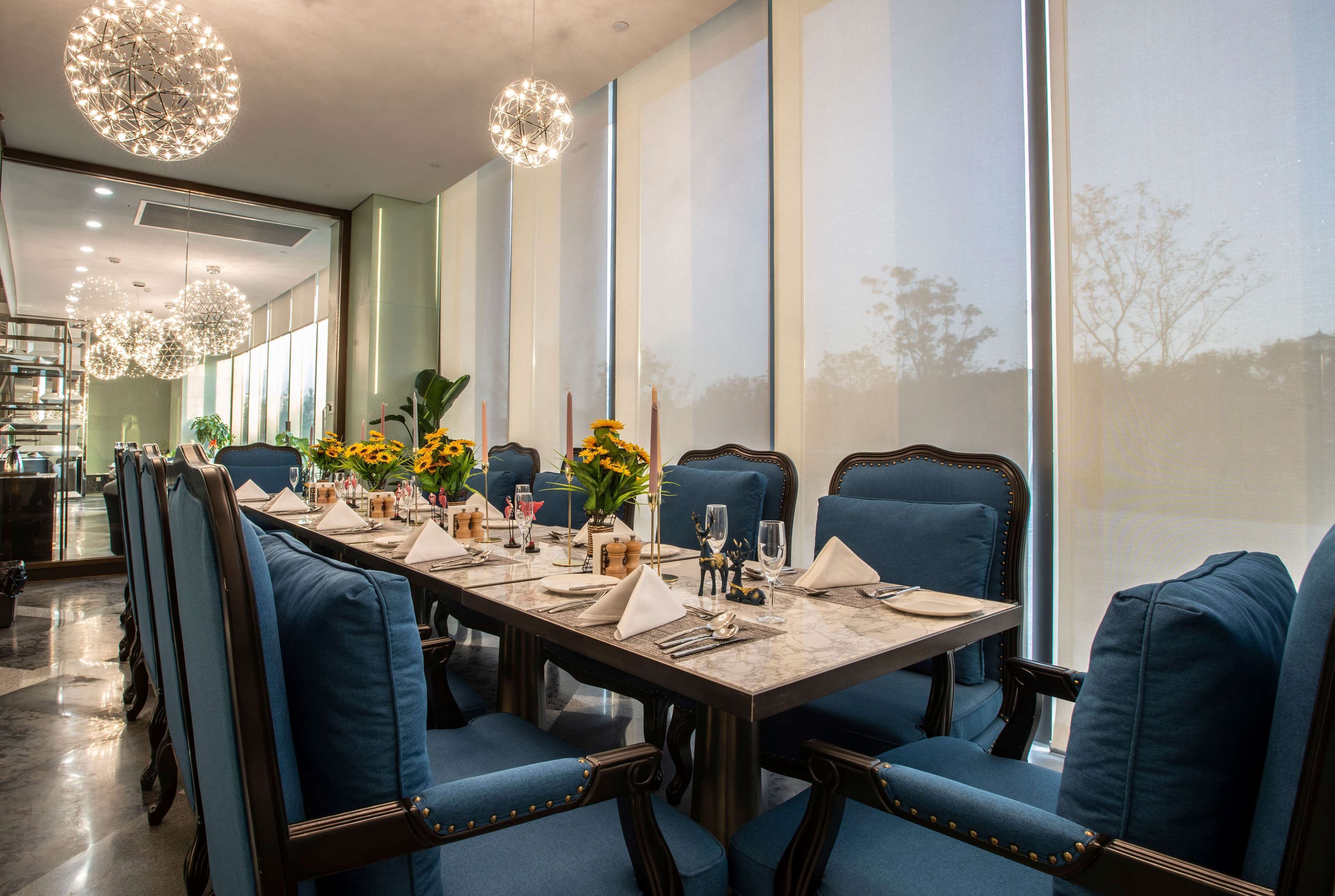 A dining area with a long table set for a meal, blue upholstered chairs, and decorative lighting.