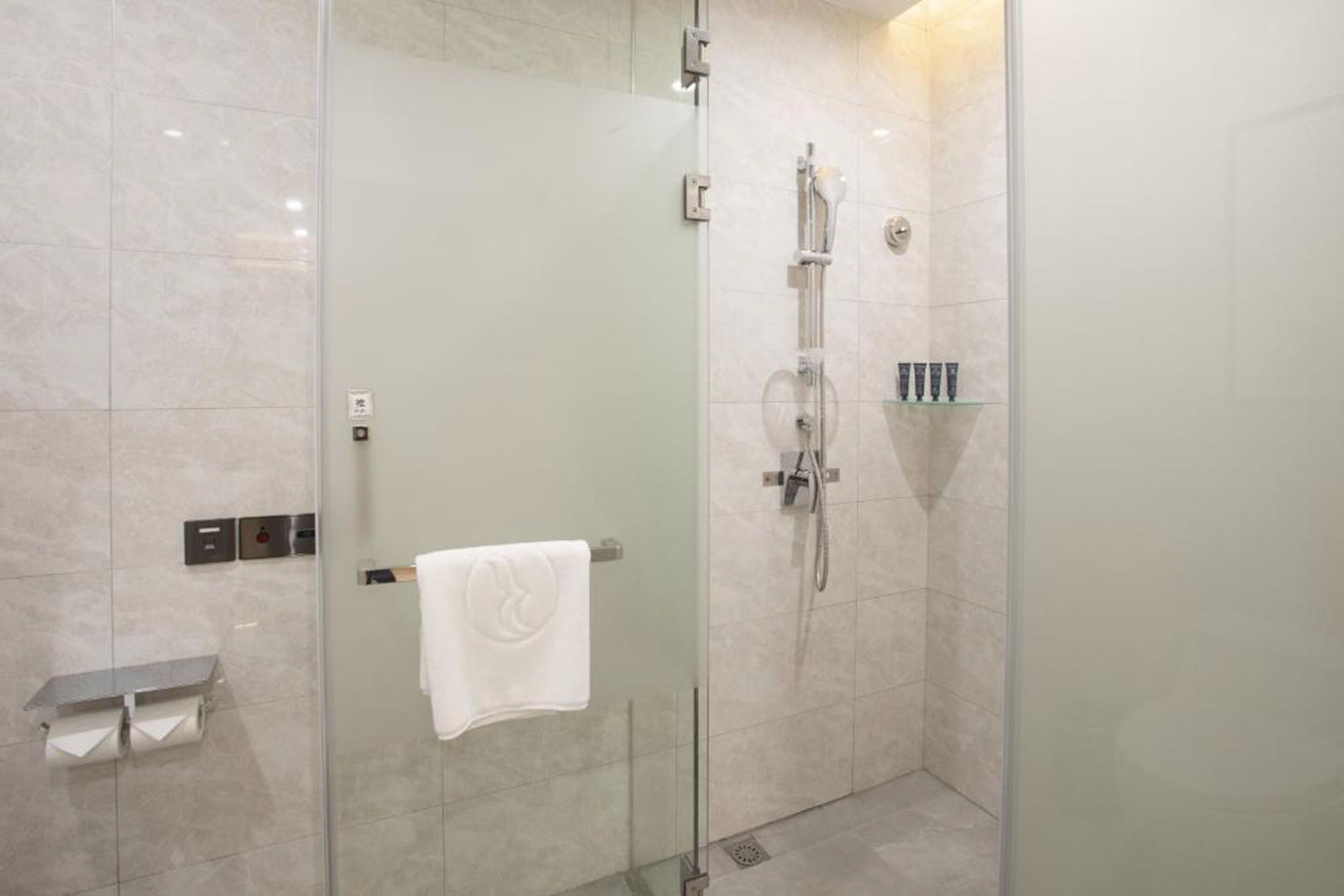 A modern bathroom with a glass-enclosed shower, a towel rack, and a shelf with toiletries.