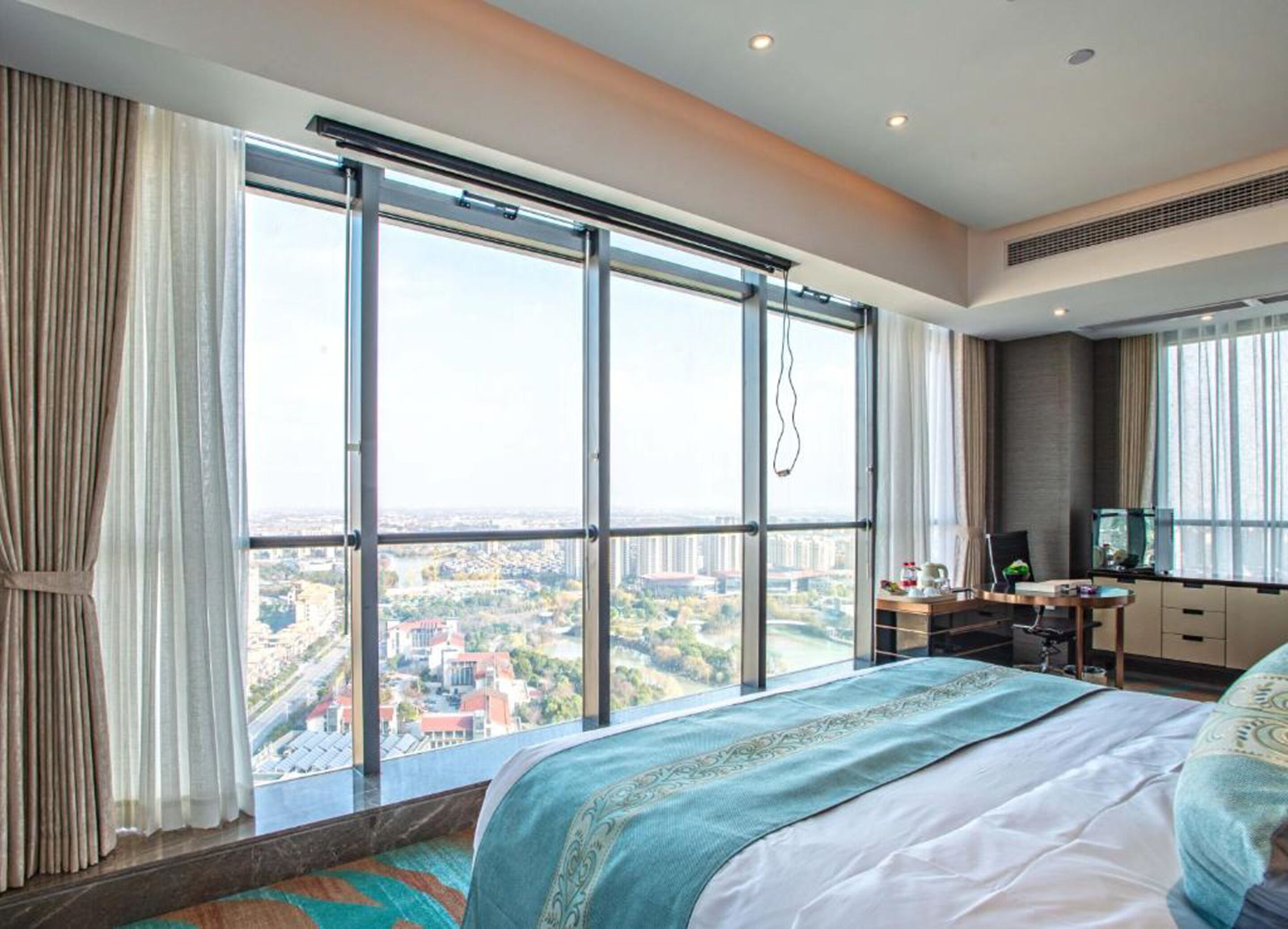 Hotelkamer met een groot raam dat uitzicht geeft op de stad, een bed met een decoratieve spreidek, een bureau met een computer en een televisie.