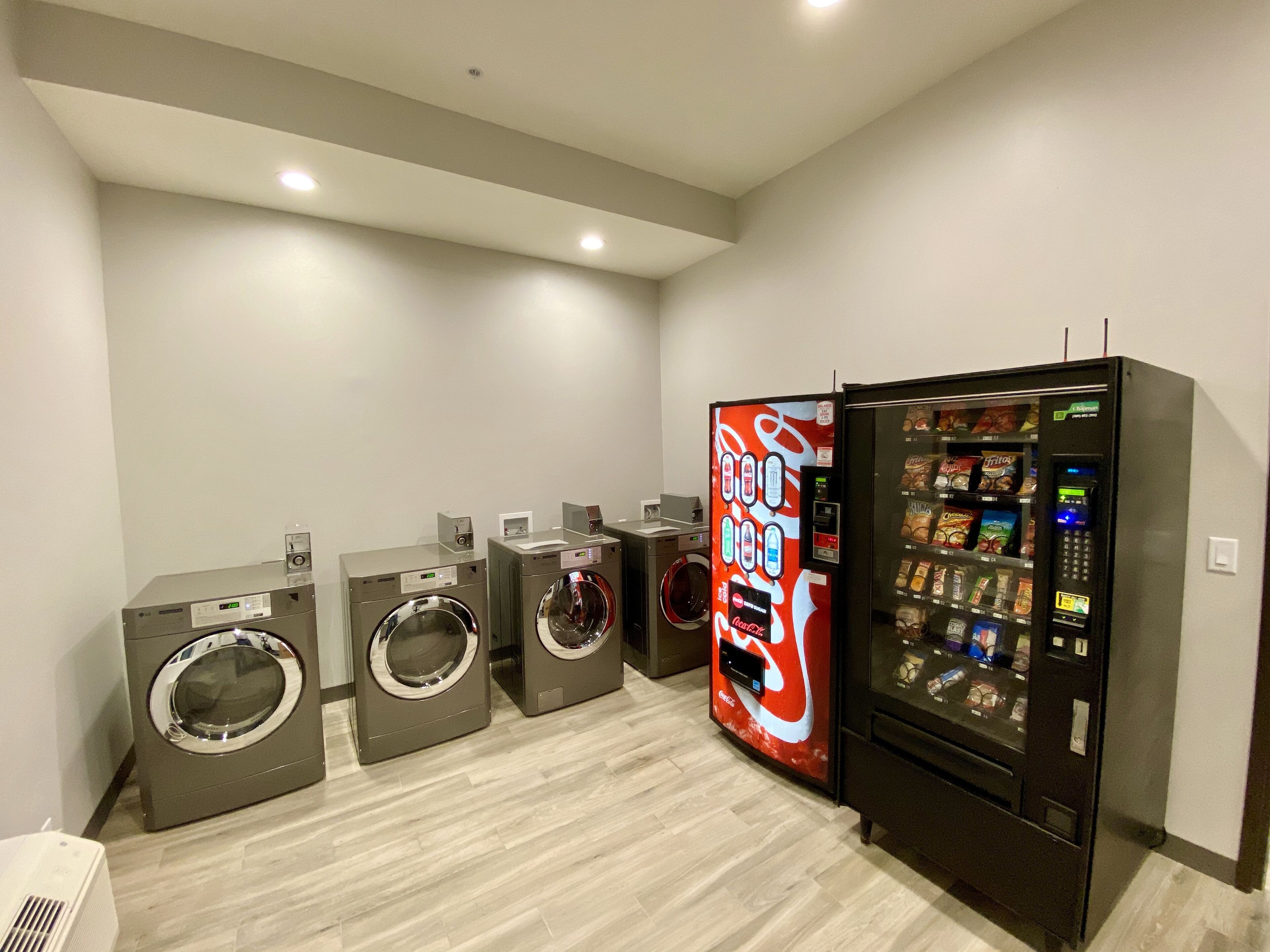 A laundry room with four washing machines and a vending machine.