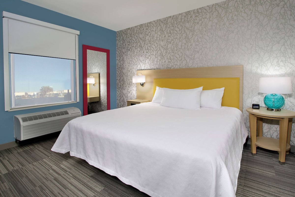 A hotel room with a large bed, a window with a view, a heater, and a nightstand with a lamp and a globe.