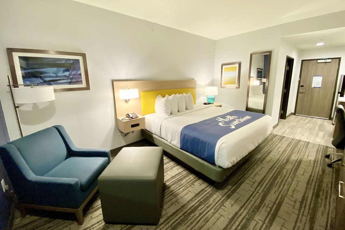 A hotel room with a bed, a desk, a chair, and a small ottoman.