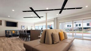 Un vestíbulo de hotel moderno con un sofá grande, zona de comedor y amplias ventanas que ofrecen vistas al exterior.