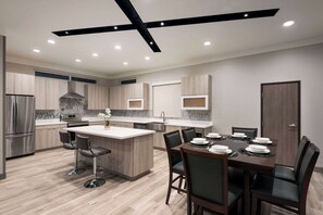 A modern kitchen with a central island, bar stools, and a dining table set for six.