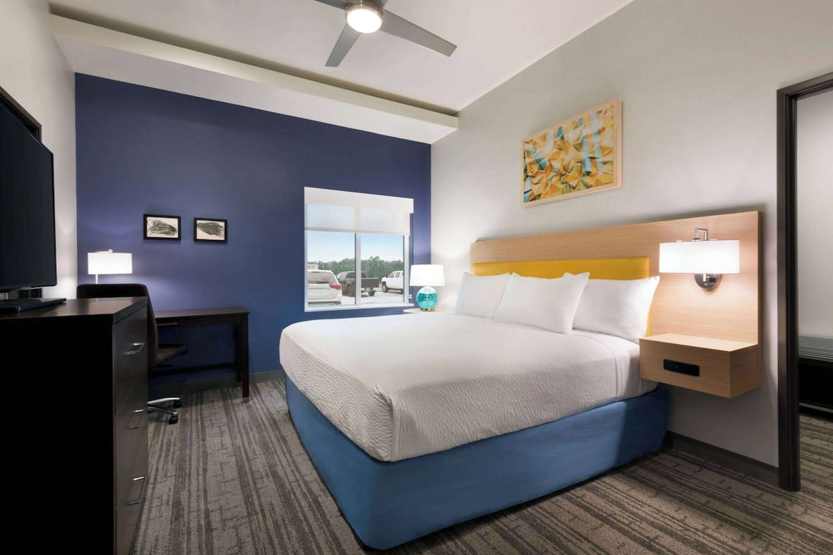 A hotel room with a bed, desk, chair, and a window with a view of the outside.
