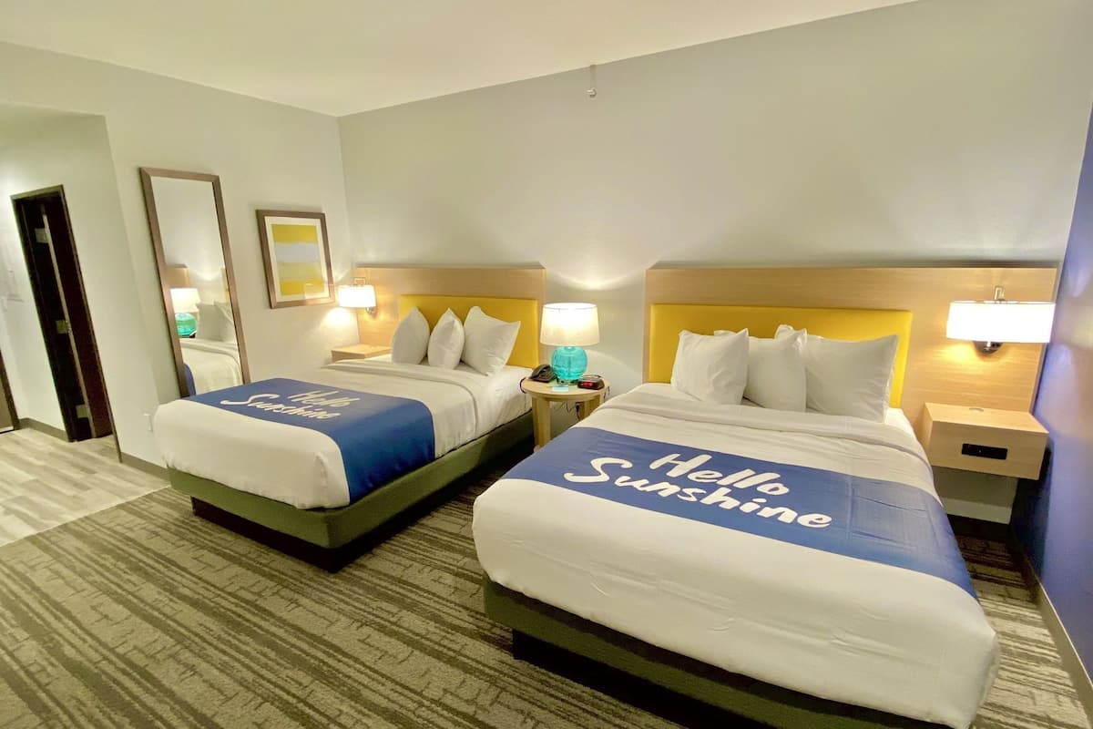 Two hotel beds with 'Hello Sunshine' bedspreads, bedside lamps, and a carpeted floor.