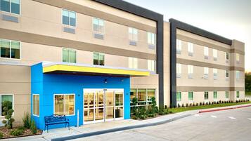 A modern building with a blue entrance, multiple windows, and a parking lot.