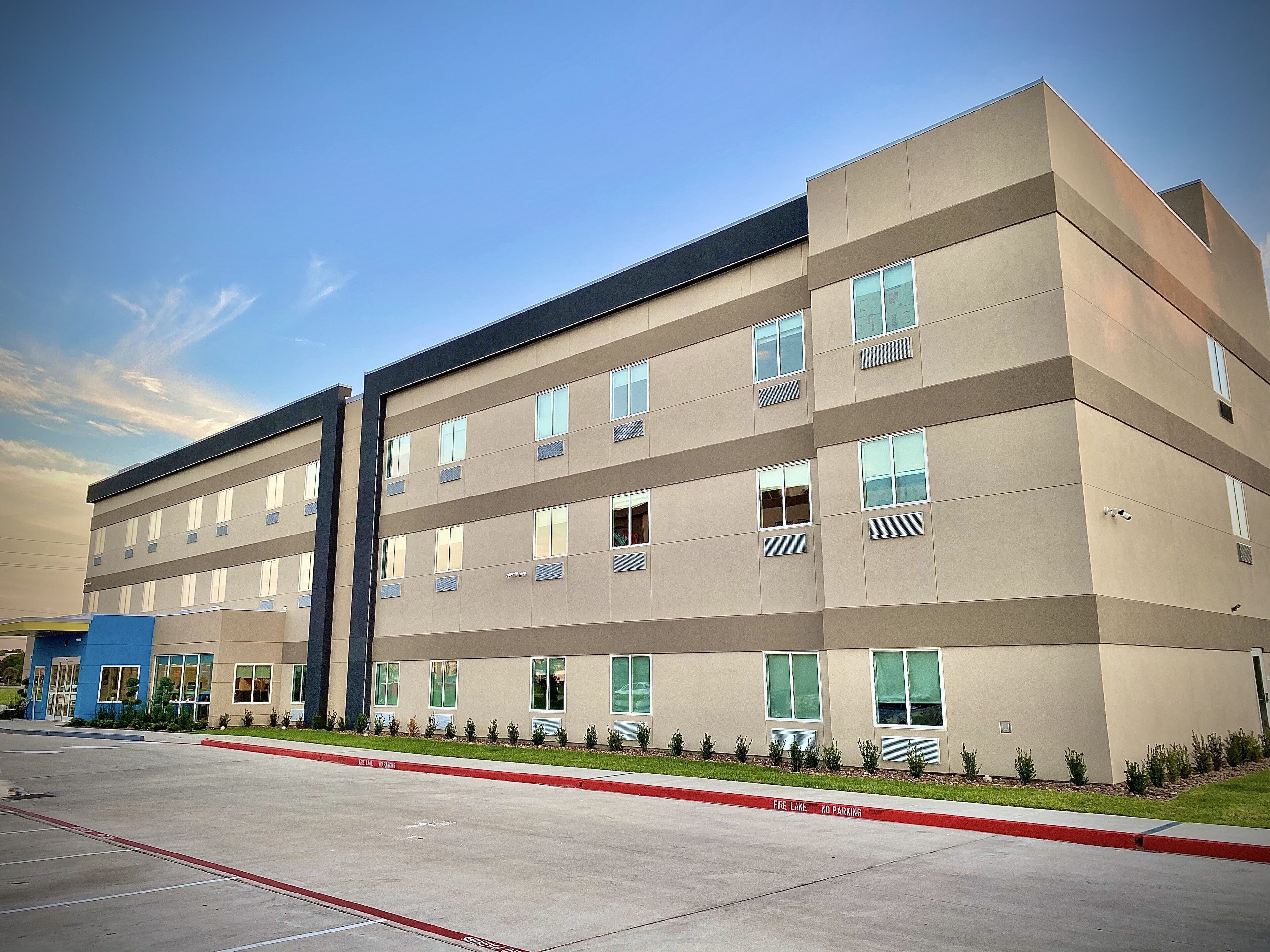 A multi-story building with a flat roof, large windows, and a fire lane marked with red paint.