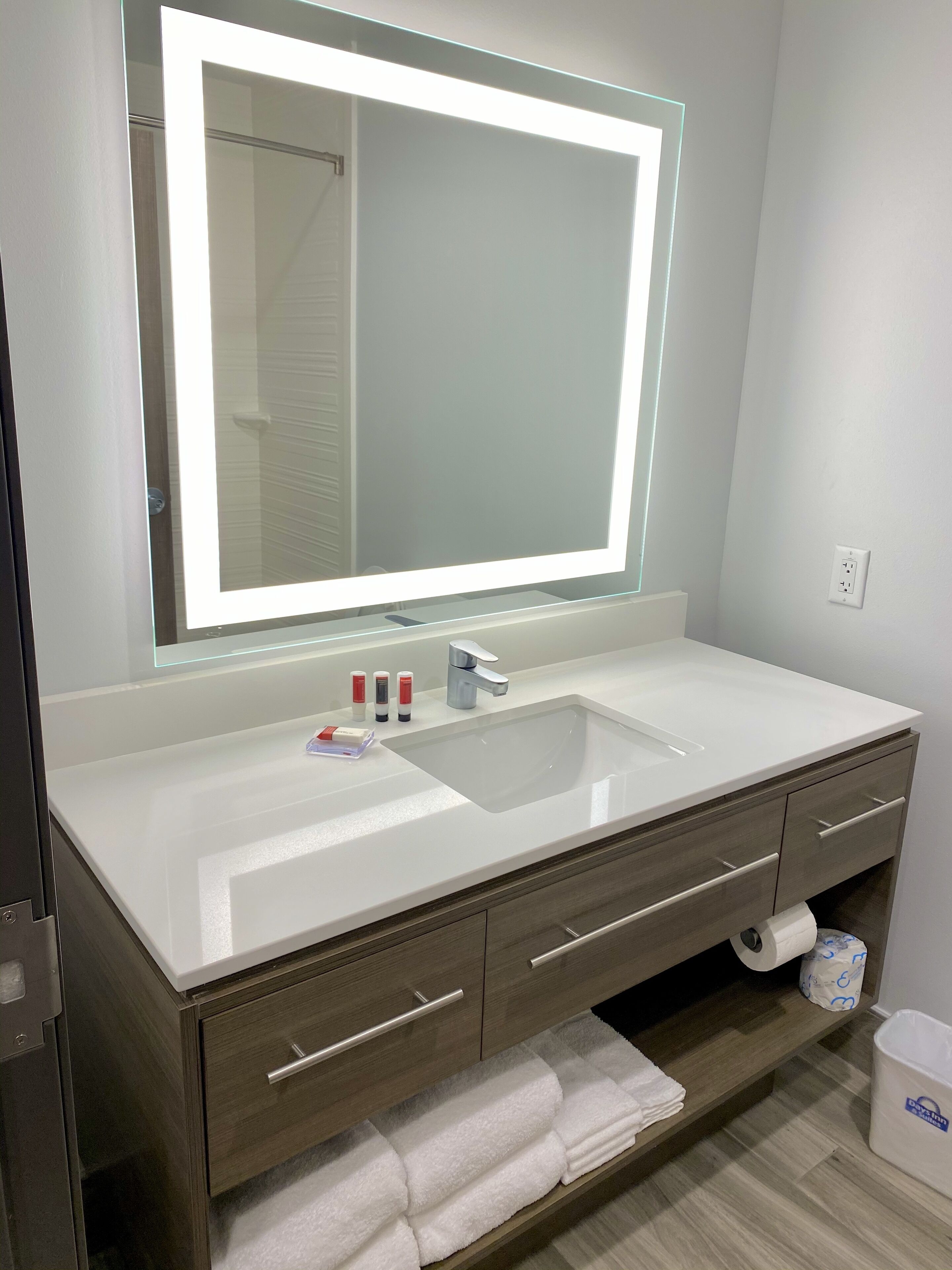 Une salle de bain moderne avec un grand miroir, un lavabo blanc et un meuble-lavabo en bois.