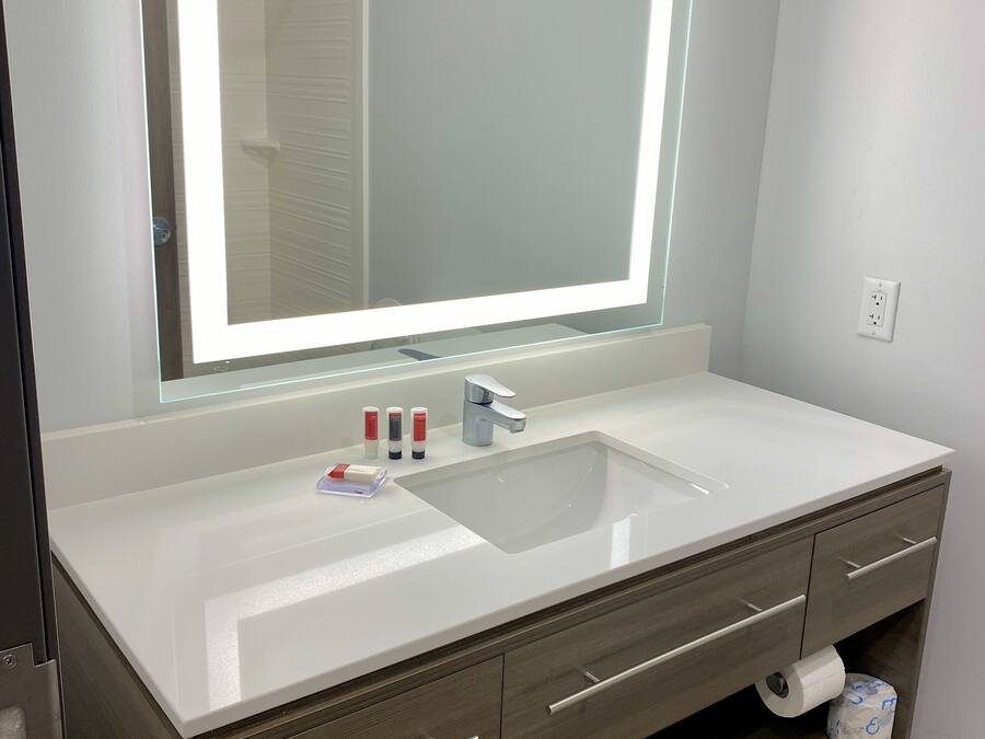 A modern bathroom with a large mirror, white sink, and wooden vanity.