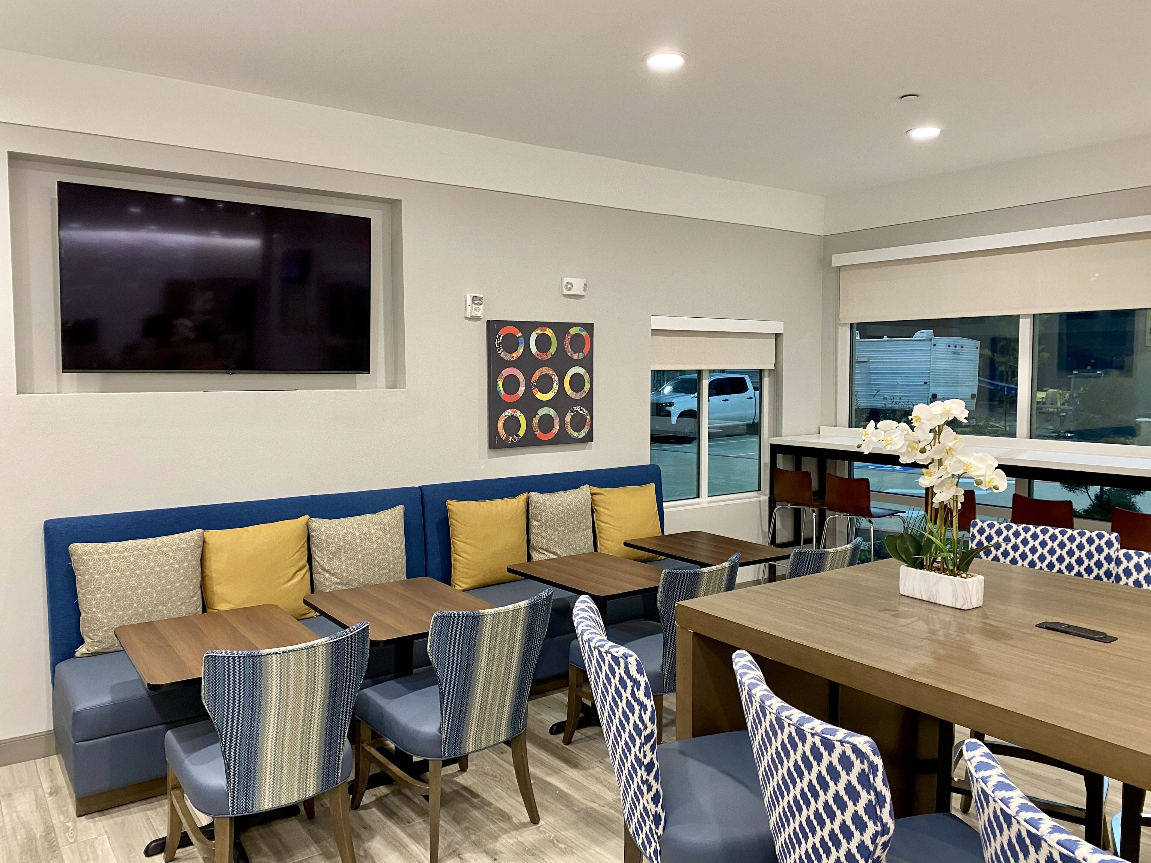 Uma sala de jantar moderna com uma mesa grande, cadeiras estampadas em azul e branco, e um sofá azul com almofadas amarelas.