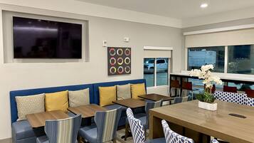 Uma sala de jantar moderna com uma mesa grande, cadeiras estampadas em azul e branco, e um sofá azul com almofadas amarelas.